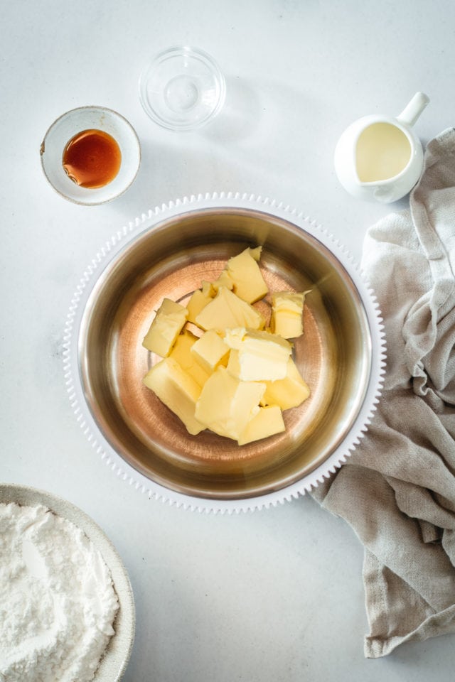 Overhead view of butter in mixing bowl with frosting ingredients in background