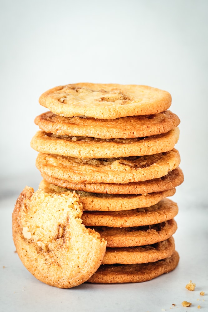 Stack of cinnamon roll cookies with one leaning against them with two bites taken out.