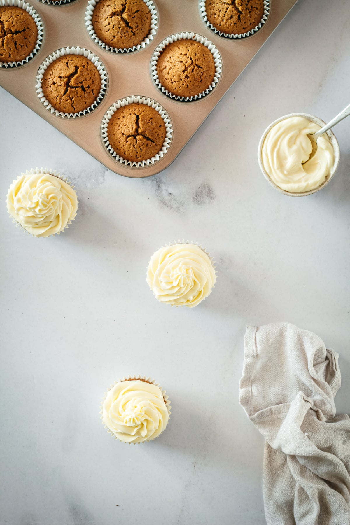 Overhead view of 3 frosted cupcakes with unfrosted cupcakes in background