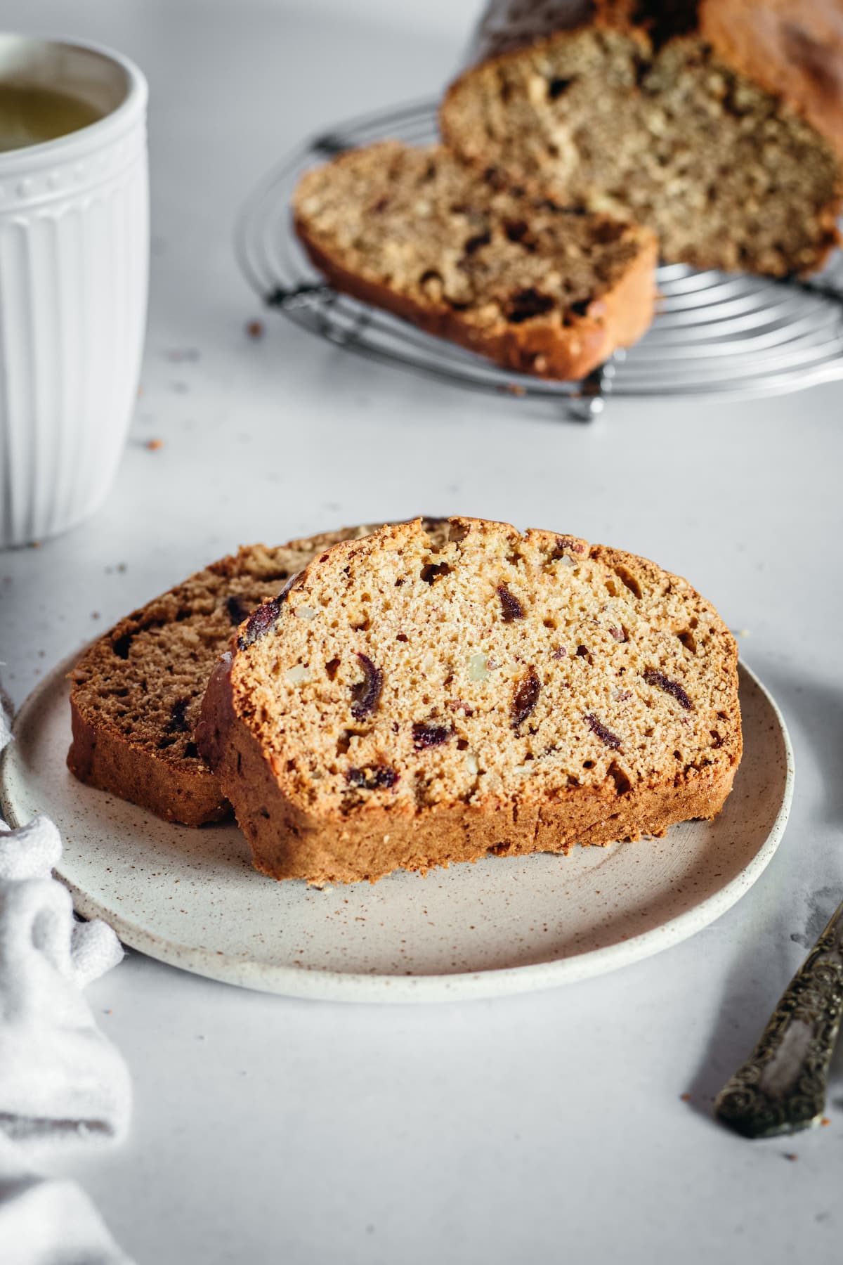 Plate with two slices of date nut bread, with remaining bread in background.