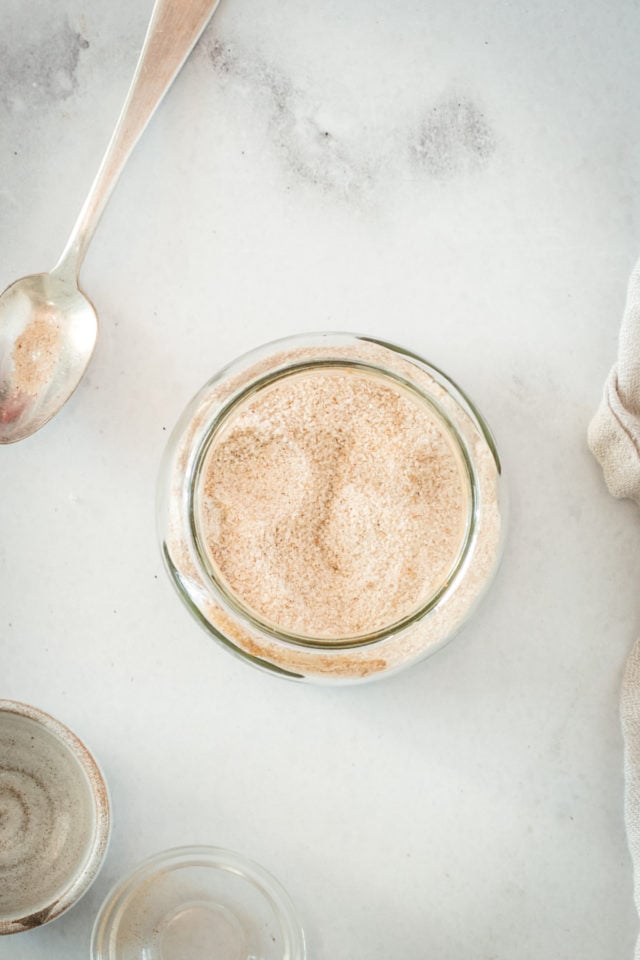 Overhead view of glass jar filled with cinnamon sugar and spoon