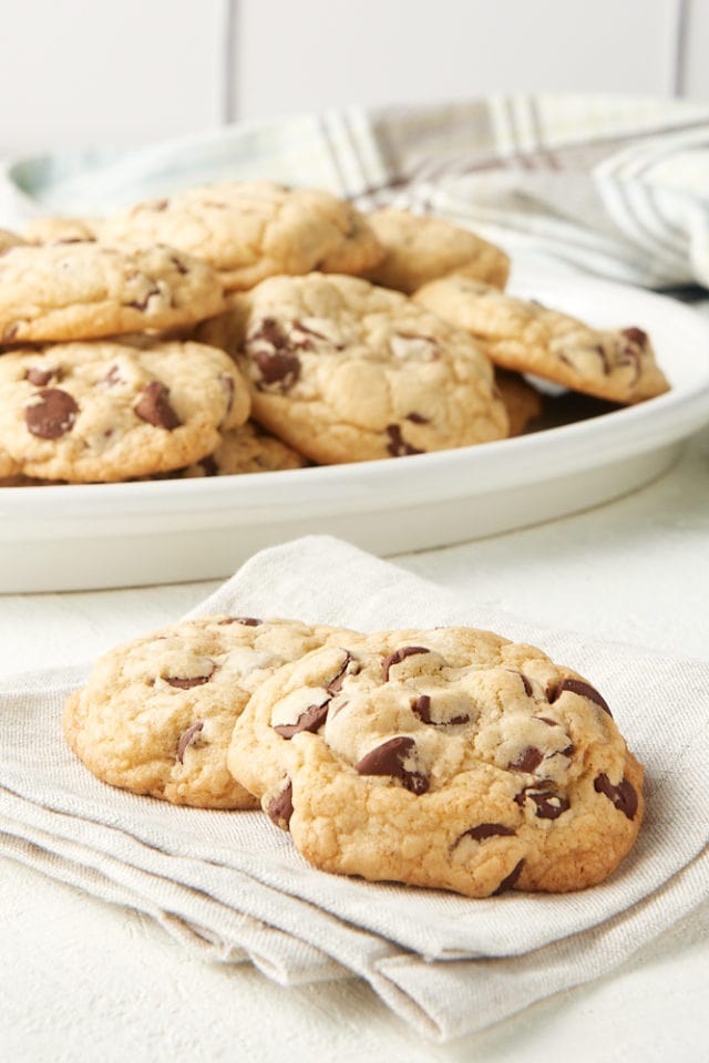 chocolate chip cookies on a beige napkin with more cookies on a tray in the background