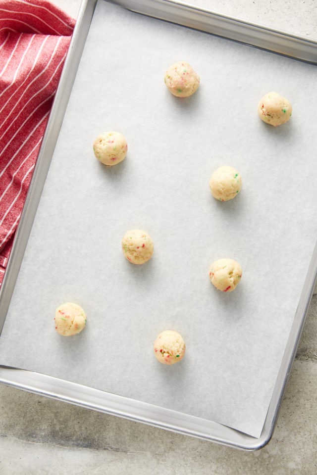 Overhead view of sugar cookie dough balls on a parchment-lined baking sheet.