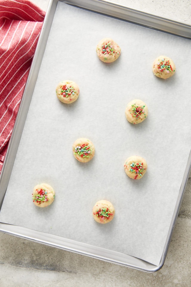 Overhead view of sugar cookie dough topped with sprinkles on a parchment-lined baking sheet.
