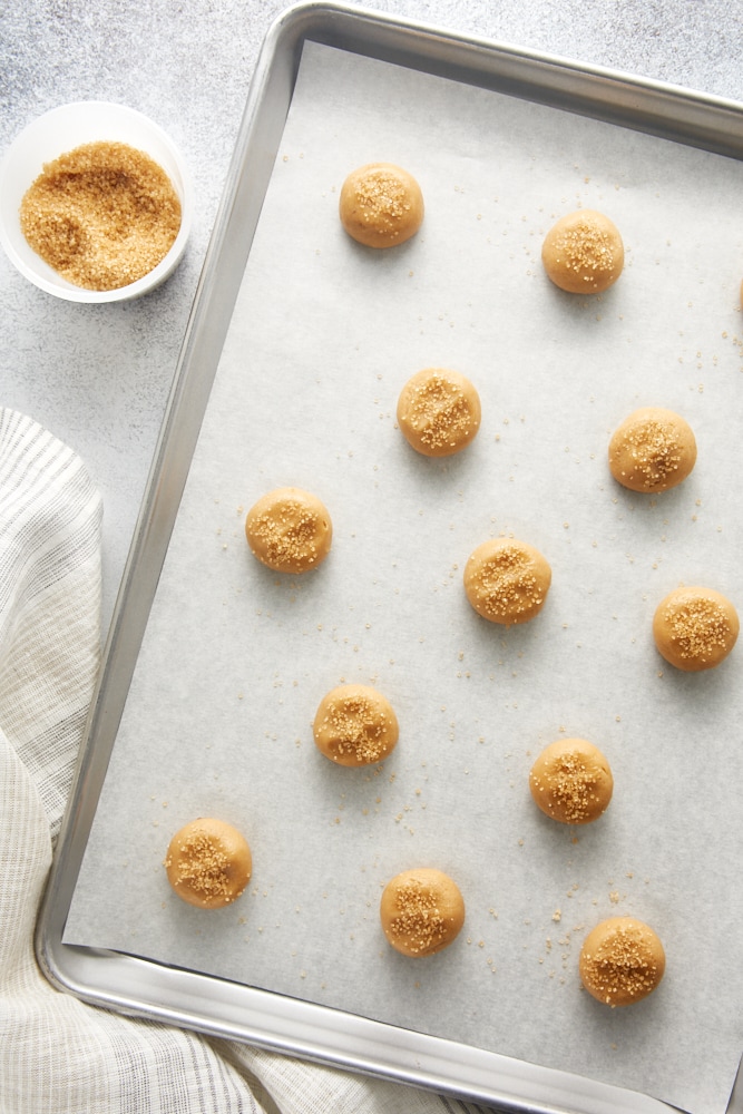 overhead view of Maple Ginger Cookie dough balls sprinkled with turbinado sugar on a parchment-lined baking sheet