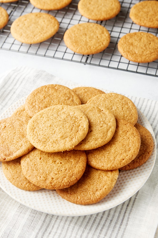 Maple Ginger Cookies on a white plate with more cookies on a wire rack in the background