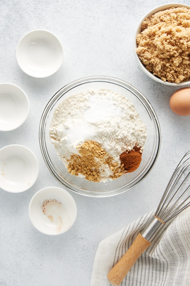 overhead view of flour, baking soda, ginger, cinnamon, and salt in a glass mixing bowl