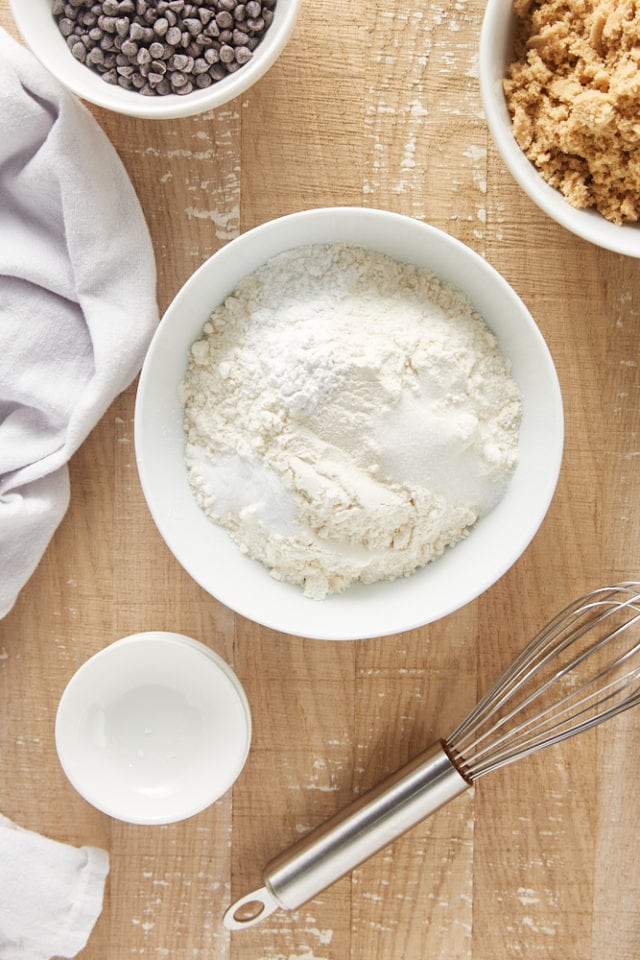 Overhead view of flour, baking powder, baking soda, and salt in a white mixing bowl.