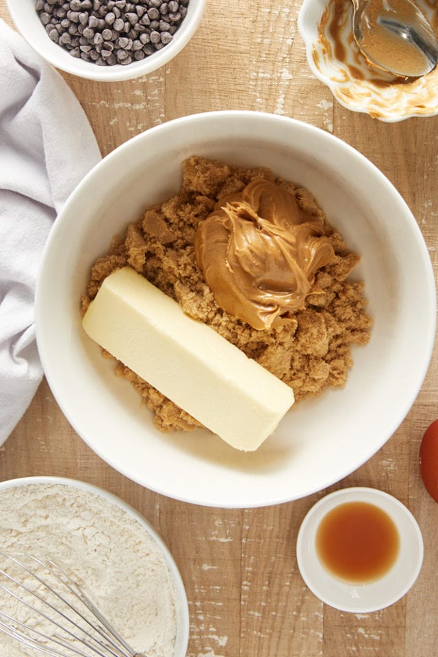 Overhead view of butter, peanut butter, and brown sugar in a white mixing bowl.