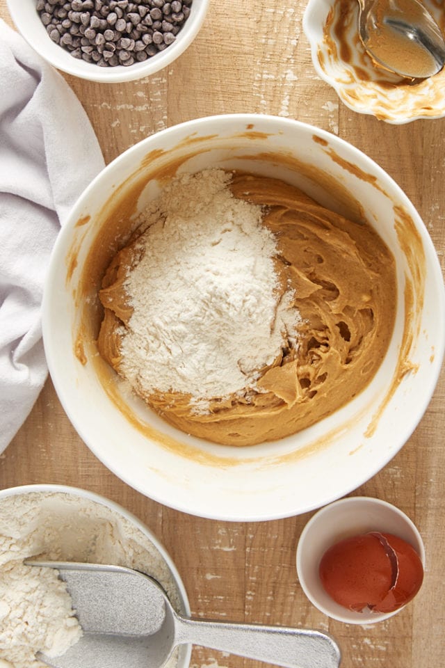 Overhead view of dry ingredients added to cookie dough in a white mixing bowl.