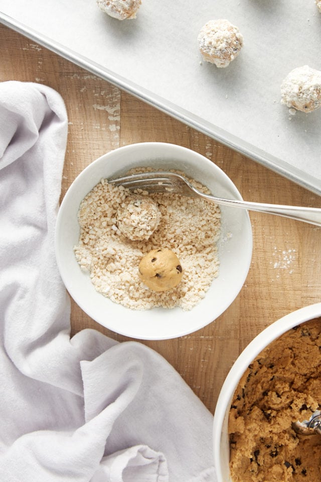 Overhead view of peanut butter crinkle cookie dough balls being rolled in a sugar and potato chip coating.