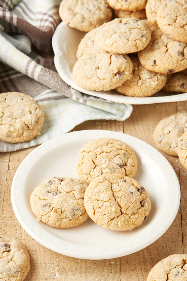 Three peanut butter crinkle cookies on a white plate with more cookies on a tray behind.