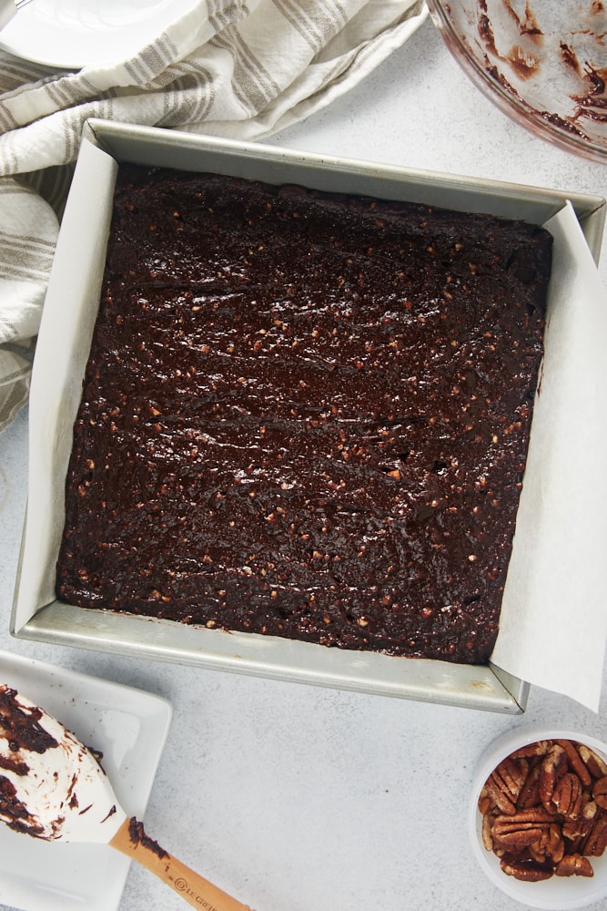 overhead view of brownie batter spread in a parchment-lined square baking pan
