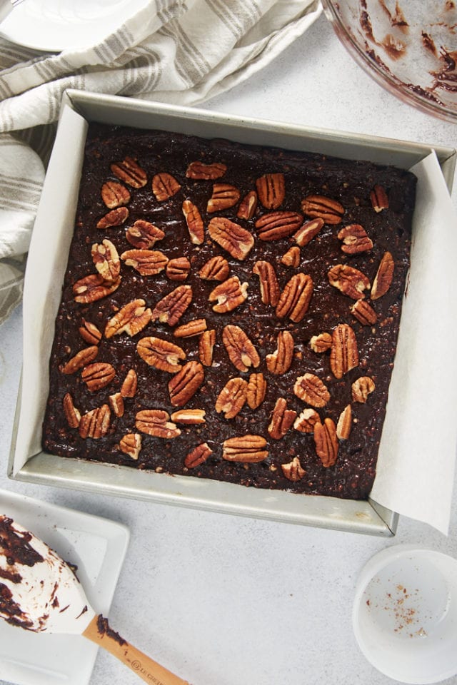 overhead view of pecans sprinkled over brownie batter in a parchment-lined baking pan