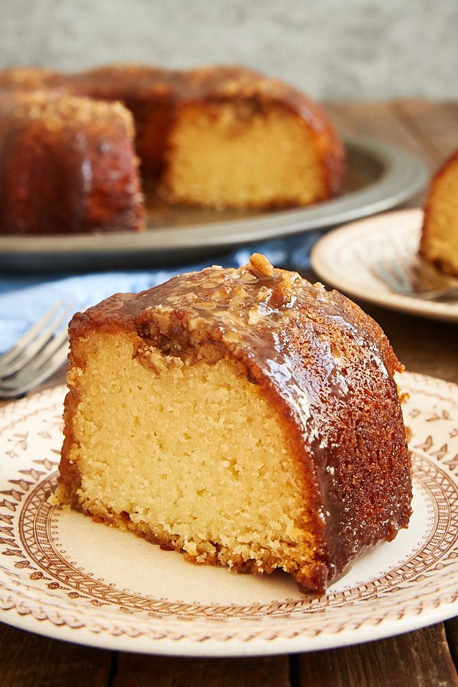 slice of Pecan Pie Bundt Cake on a brown floral plate with the remaining cake in the background