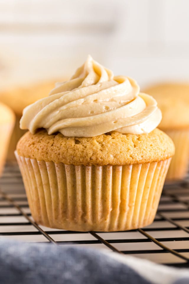 a frosted Brown Sugar Pound Cake on a wire rack with more unfrosted cakes in the background