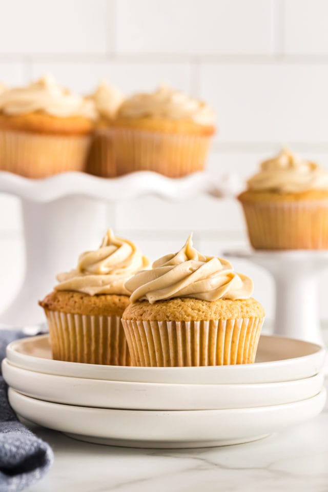 two Brown Sugar Pound Cakes on a stack of white plates with more cakes on white pedestals in the background