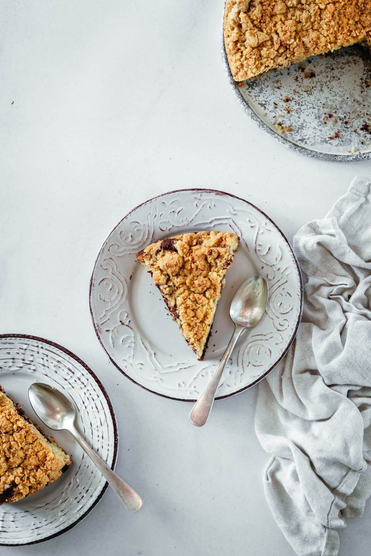 Overhead view of two plates of coffee cake with spoons, with remaining coffee cake in background