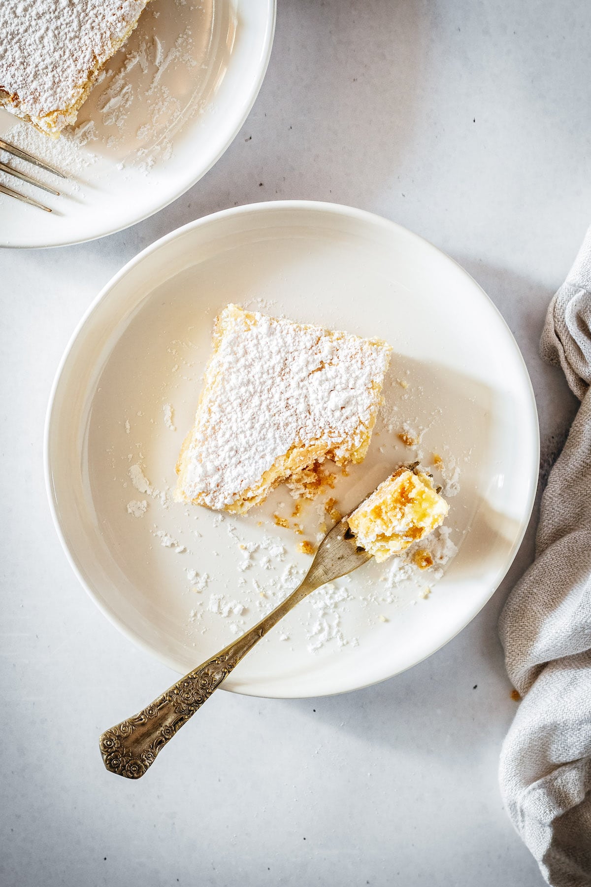 Lemon bar on plate with fork; fork has piece of bar on it