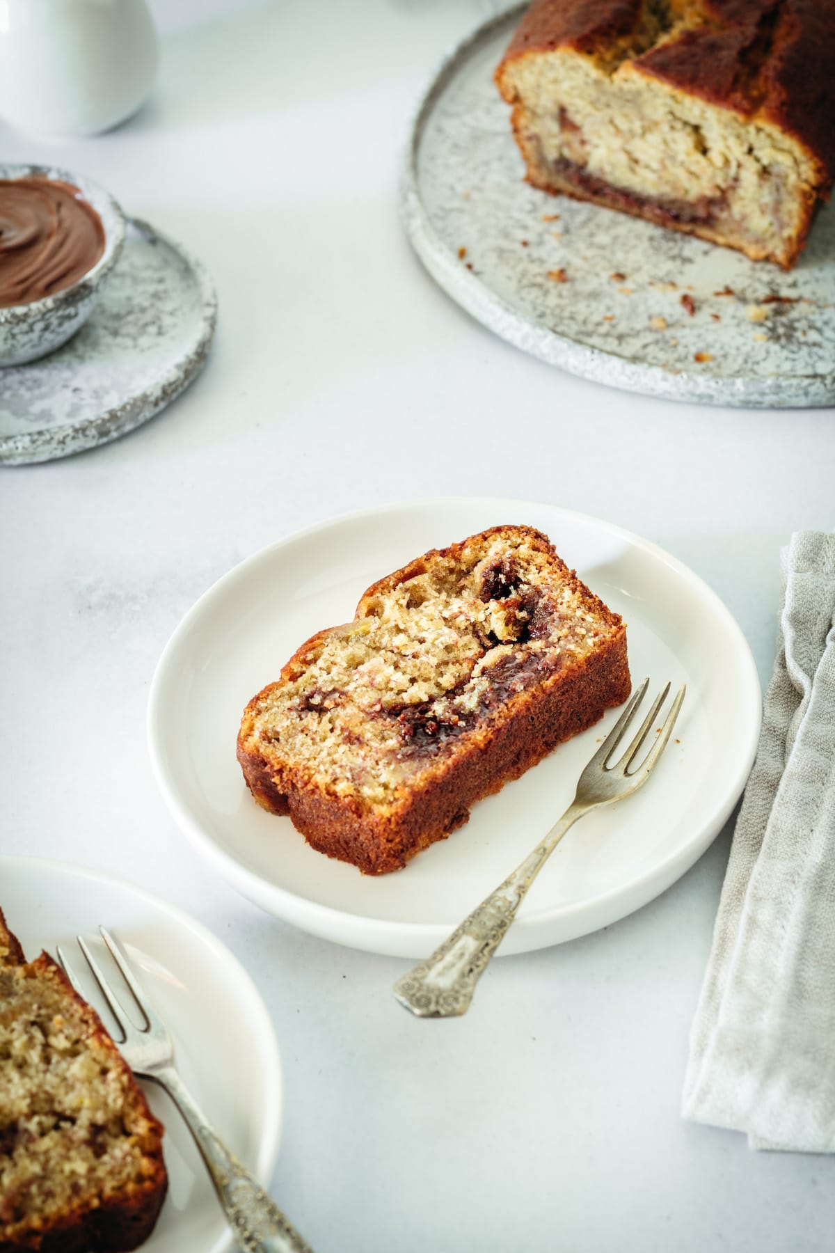 Nutella banana bread slice on plate with fork, with remaining loaf in background