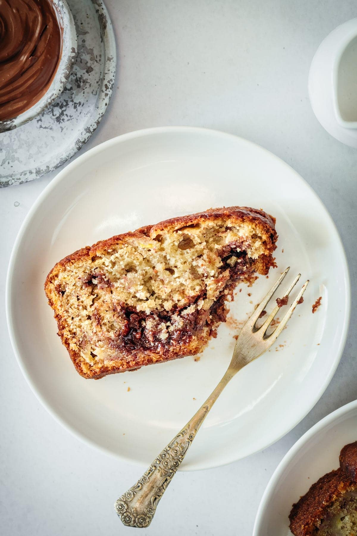 Overhead view of Nutella Banana Bread slice on plate with fork, with corner eaten