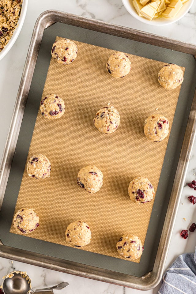 Overhead view of portioned oatmeal cranberry cookie dough on a silicone-lined baking pan.