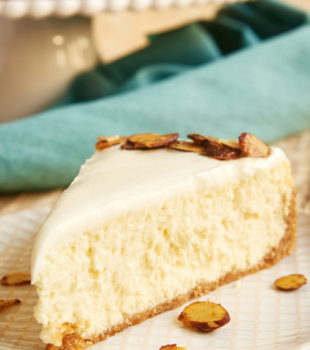 slice of Amaretto Cheesecake topped with candied almonds and served on a beige and white plate