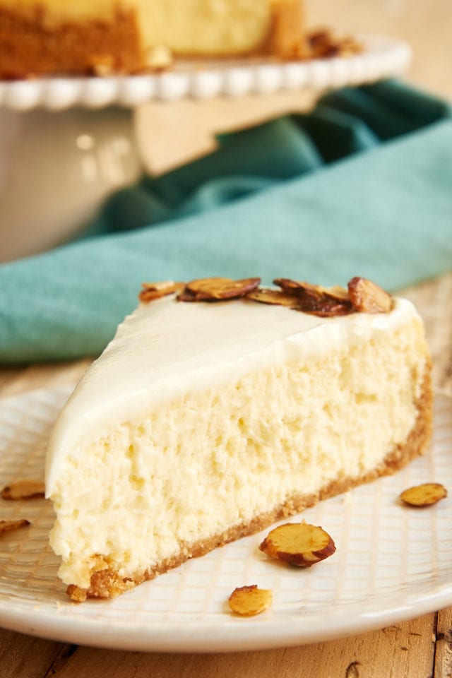 slice of Amaretto Cheesecake topped with candied almonds and served on a beige and white plate