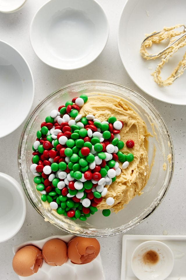 Overhead view of Christmas M&Ms added to cookie dough in a glass mixing bowl.