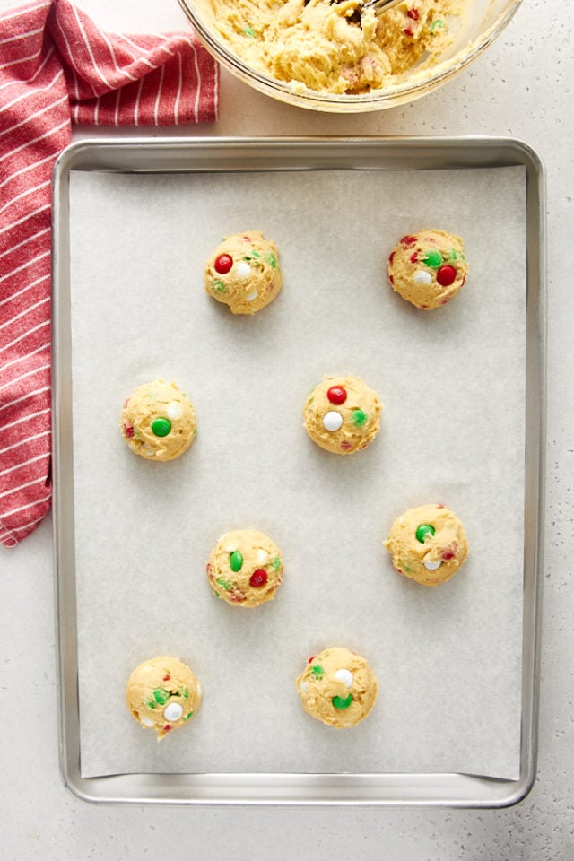 Overhead view of M&M cookie dough portioned and placed on a parchment-lined baking sheet.