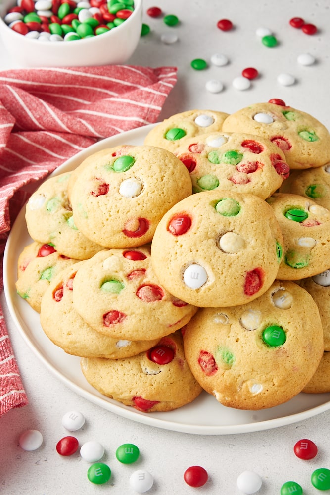 Christmas M&M Cookies piled on a white plate with M&Ms scattered around the plate