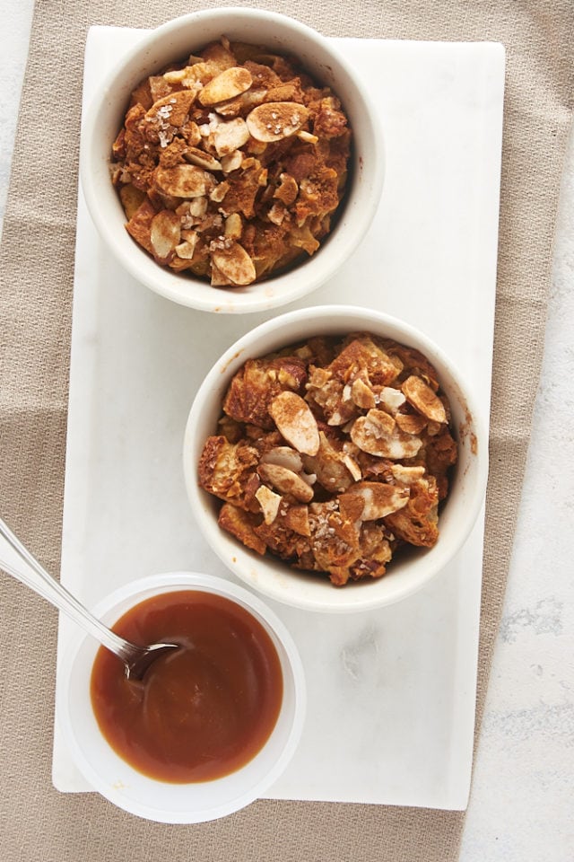 overhead view of Cinnamon Almond Bread Pudding for Two and a bowl of salted caramel on a marble tray