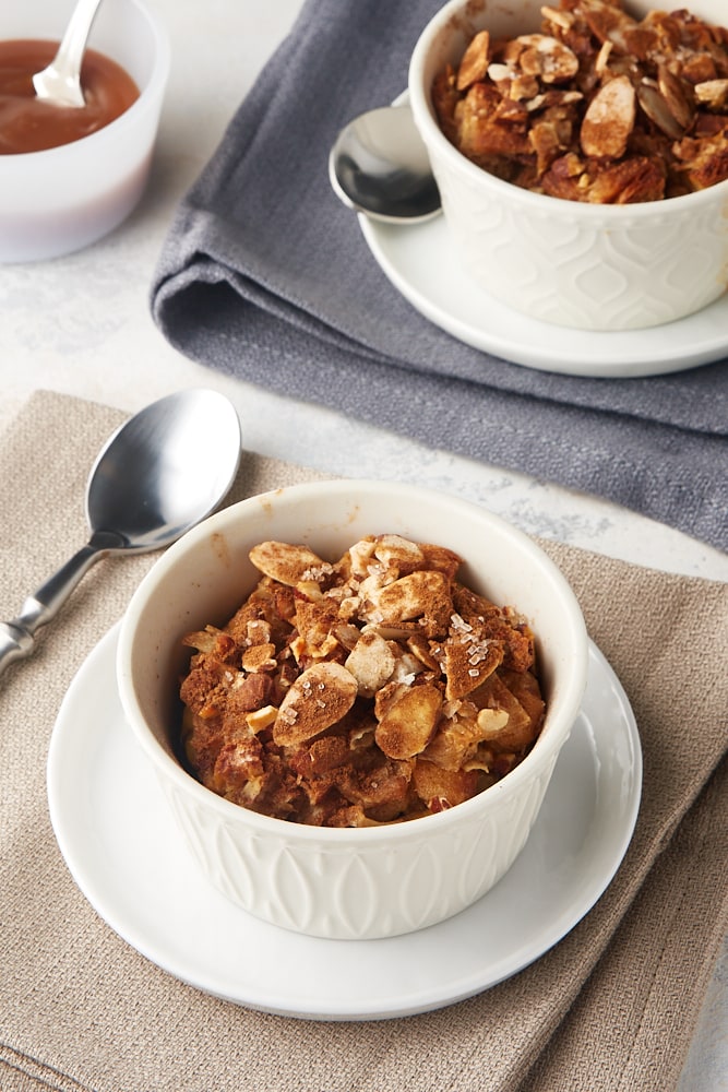 Cinnamon Almond Bread Pudding for Two in white ramekins on white plates on beige and gray napkins