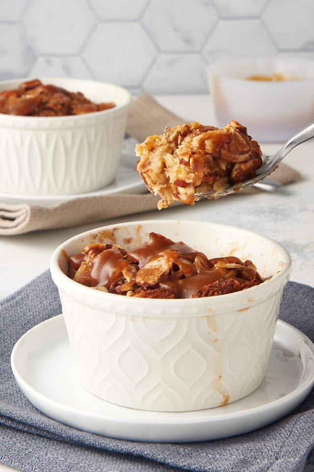 a bite of Cinnamon Almond Bread Pudding on a spoon held above the remaining bread pudding in a white ramekin