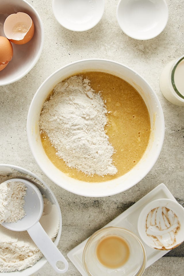 overhead view of flour added to cake batter in a white mixing bowl