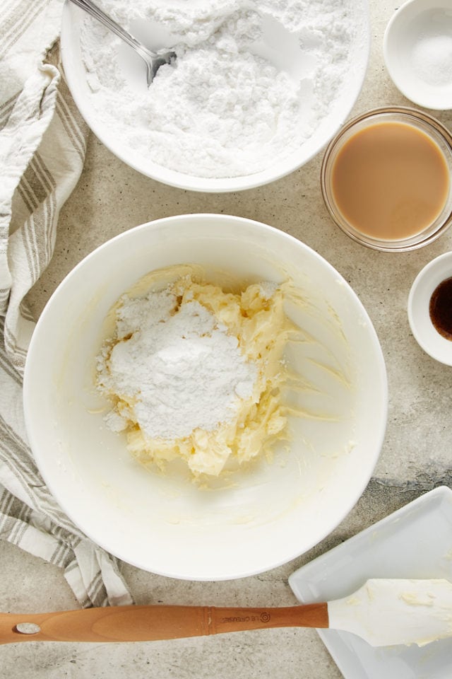 overhead view of sugar added to creamed butter in a white mixing bowl