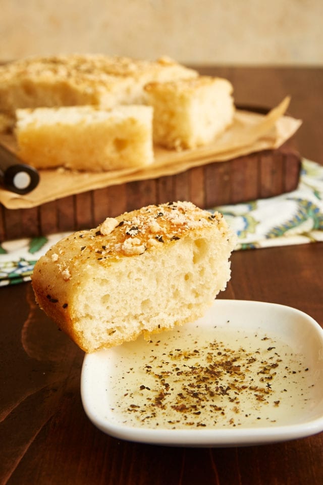 slice of No-Knead Focaccia on the rim of a small plate filled with olive oil and cracked black pepper