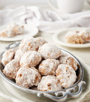 Nutty Spiced Snowball Cookies in a pewter tray on a white plate with more cookies on plates in the background