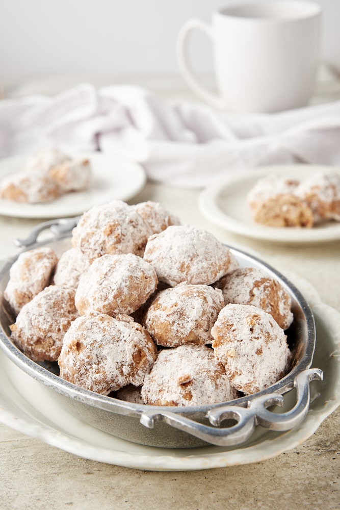 Nutty Spiced Snowball Cookies in a pewter tray on a white plate with more cookies on plates in the background