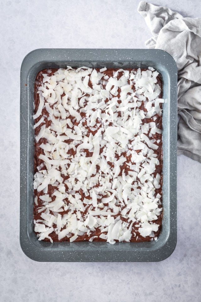 overhead view of flaked coconut sprinkled over brownie batter in a rectangular baking pan