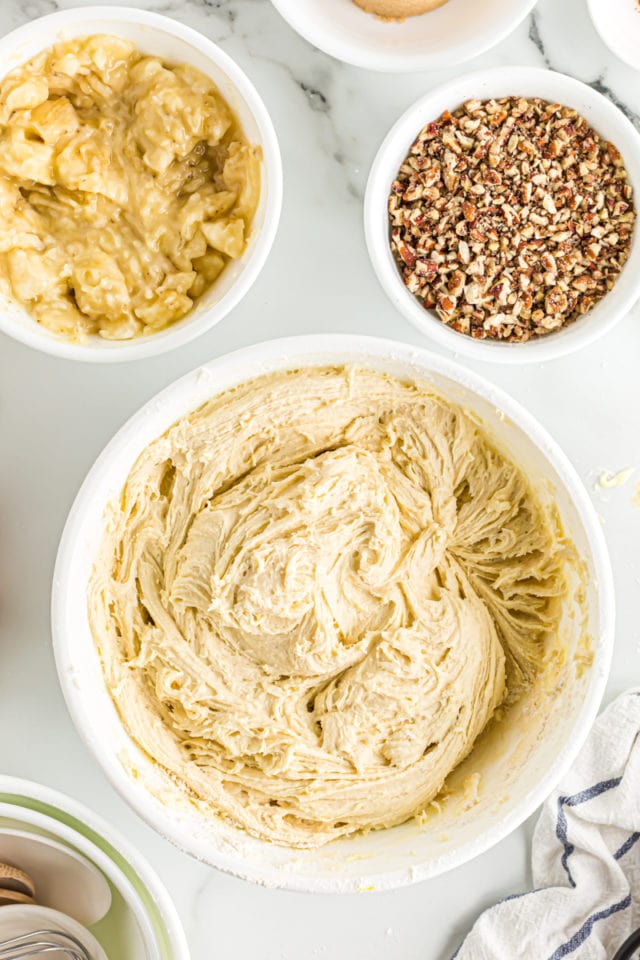 Overhead view of bowl of mashed banana, chopped pecans, and bread batter