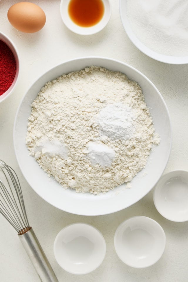 Overhead view of flour, baking powder, baking soda, and salt in a white mixing bowl.