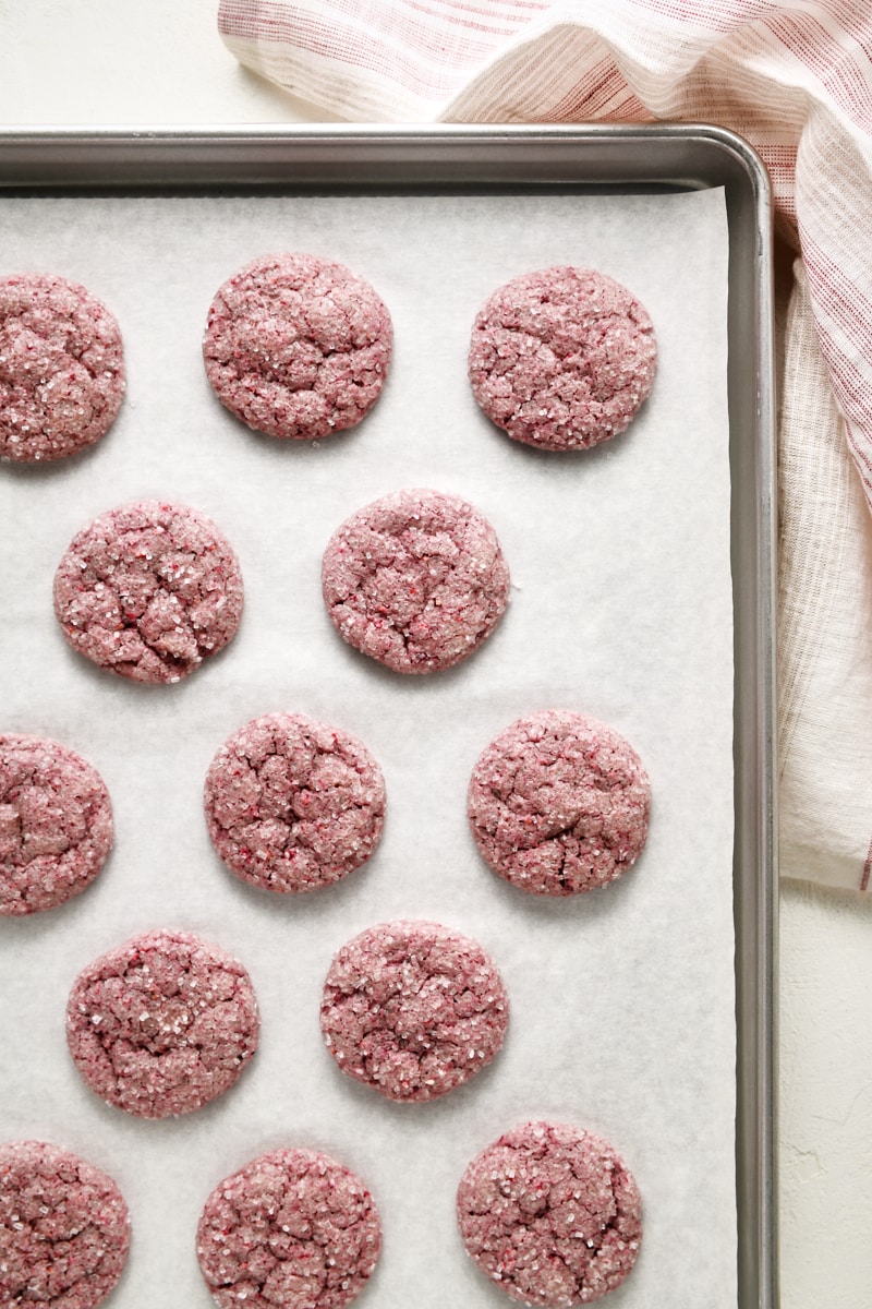 Overhead view of freshly baked raspberry sugar cookies on a parchment-lined baking sheet.