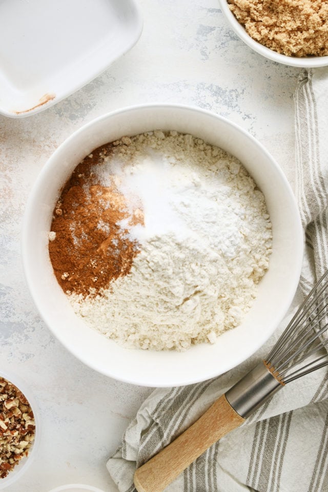 overhead view of flour, baking powder, baking soda, salt, and cinnamon in a white mixing bowl