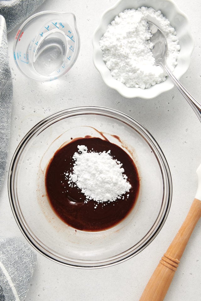 overhead view of confectioners' sugar added to melted butter and unsweetened chocolate in a glass mixing bowl