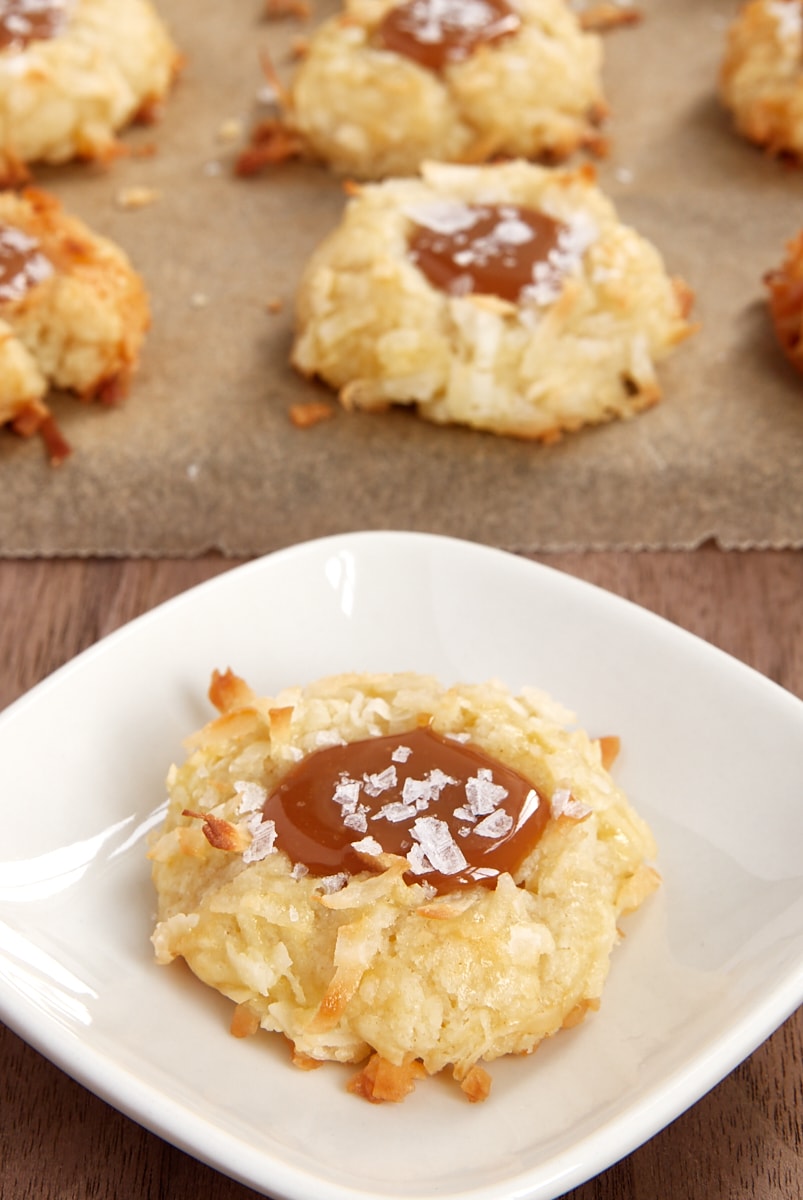 Coconut-Salted Caramel Thumbprint Cookie on a white plate with more cookies on parchment paper in the background