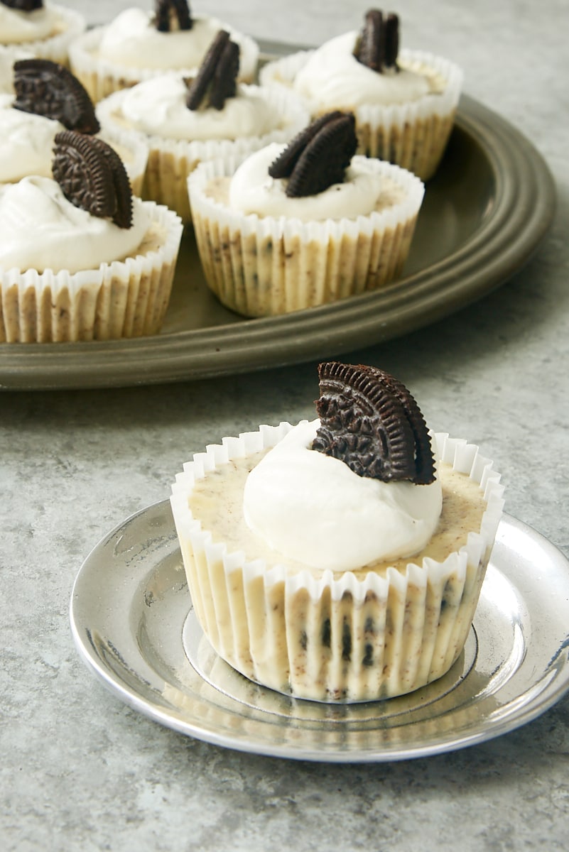 a Cookies and Cream Cheesecake on a pewter plate with more cheesecakes on a tray in the background