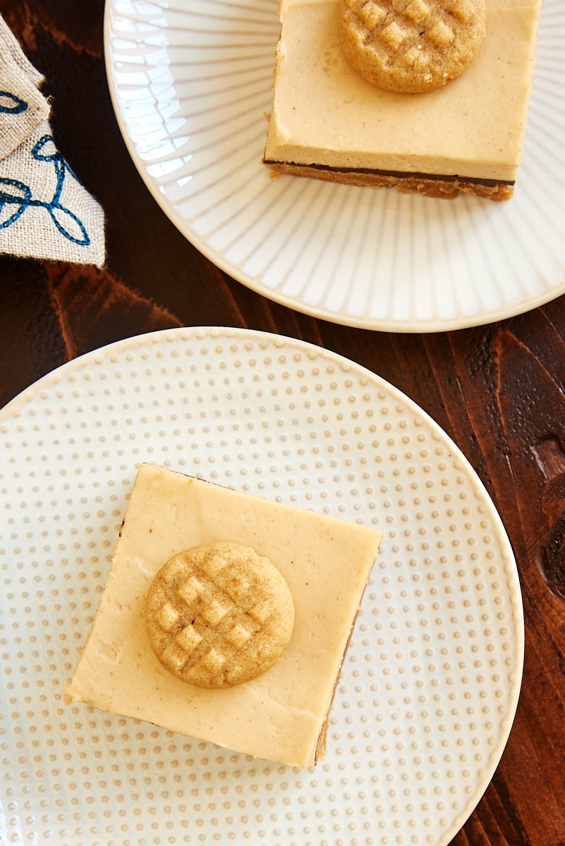 overhead view of two Peanut Butter Cheesecake Bars on white and beige plates