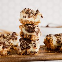 Three cookie dough cheesecake bars stacked on wood board