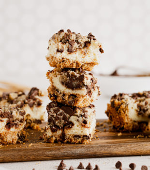 Three cookie dough cheesecake bars stacked on wood board